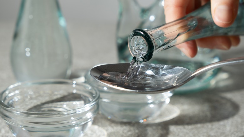 Pouring distilled white vinegar in a spoon over a bowl