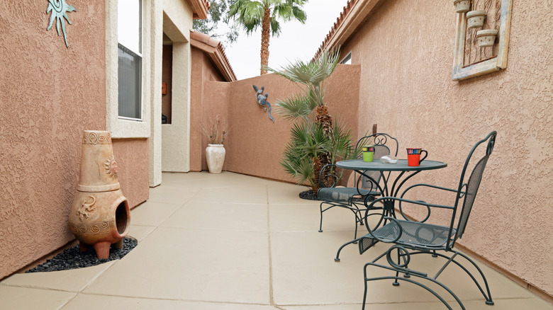 A stucco patio area in a small backyard with a fireplace and a metal table and chairs.