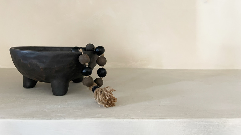 A garland made from paper mache beads and a tassel cascades from a wooden bowl sitting on a mantle.