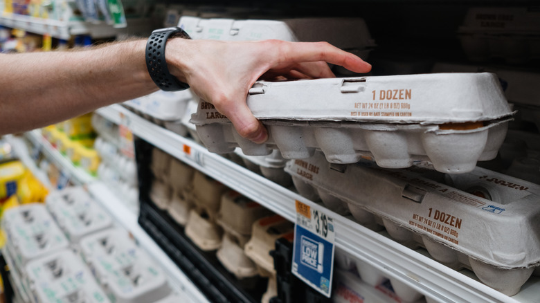 A person grabs a carton of 1 dozen eggs from the shelf at the supermarket.