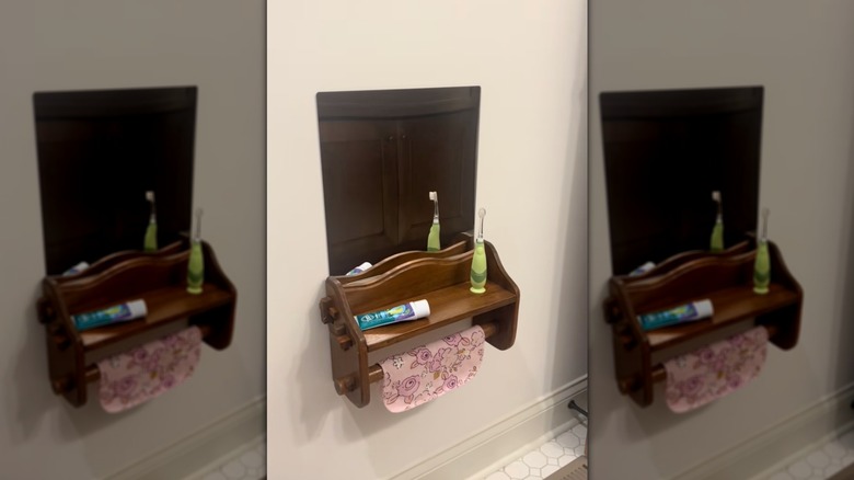 A vintage paper towel holder turned into a small bathroom vanity with a toothbrush and toothpaste on top, and a towel hanging from the rod