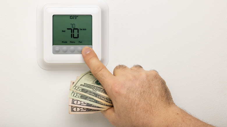 Hand holding money adjusting thermostat