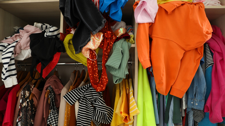 A messy closet with colorful clothes.