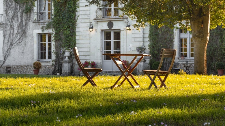 An elegant lawn table and chairs is in front of a stone chateau