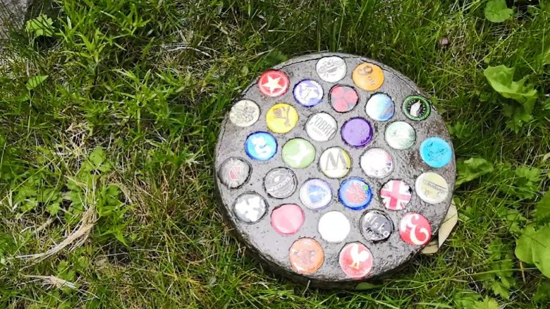 A stepping stone made with bottle caps sitting on grass.