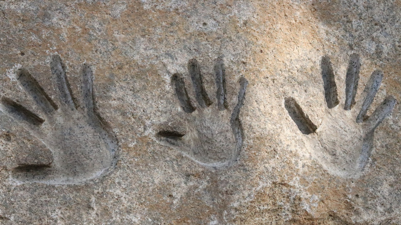 Three children handprints on a stone in the sun.