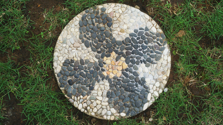 A stepping stone with different colored pebbles arranged in a flower pattern.