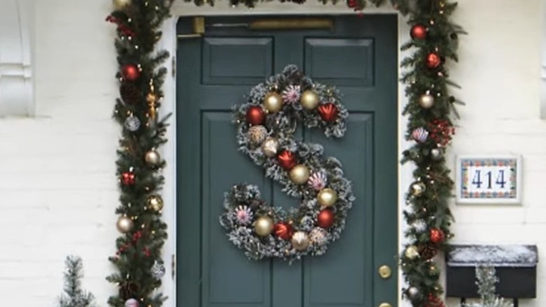 Monogram S door wreath on a dark green door surrounded by a festive garland