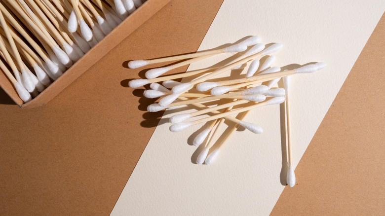 a box of Q-tips in the corner with several other Q-tips dropped in a messy stack on  brown and white surface