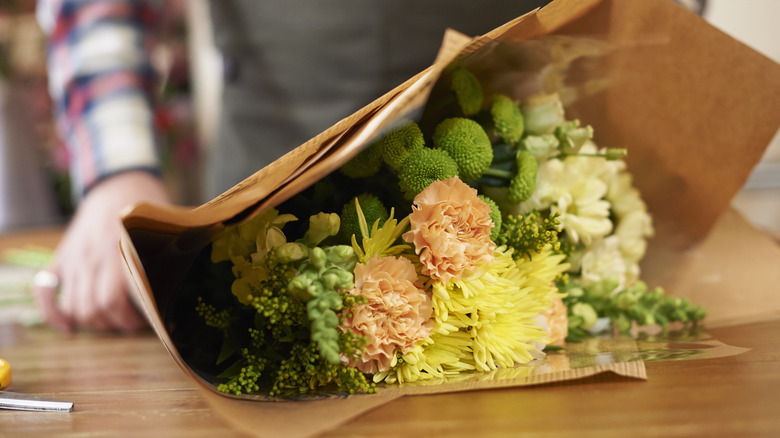A hand holding a bouquet of flowers wrapped in paper