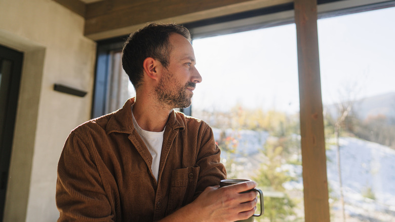 A man with a cup of coffee staring out of his sliding glass doors