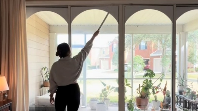 An influencer standing pointing to the cardboard arches on her sliding glass doors with a ruler.