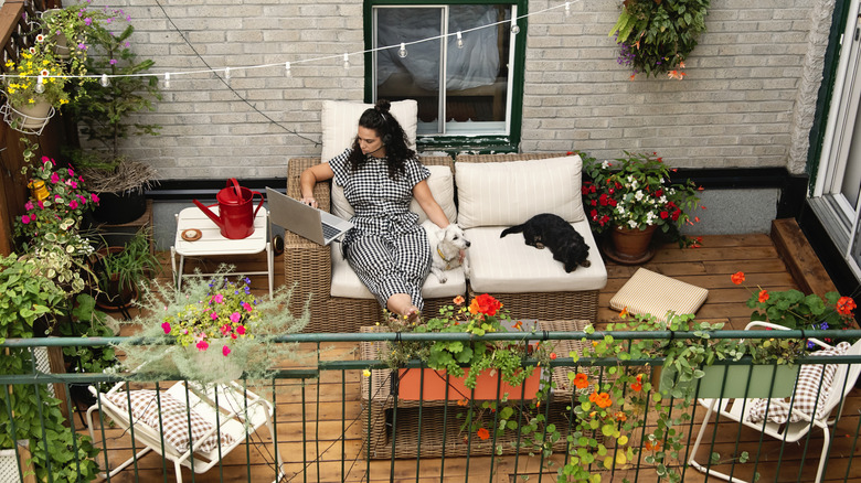 A woman sitting on her patio with her dog surrounded by flowering plants.