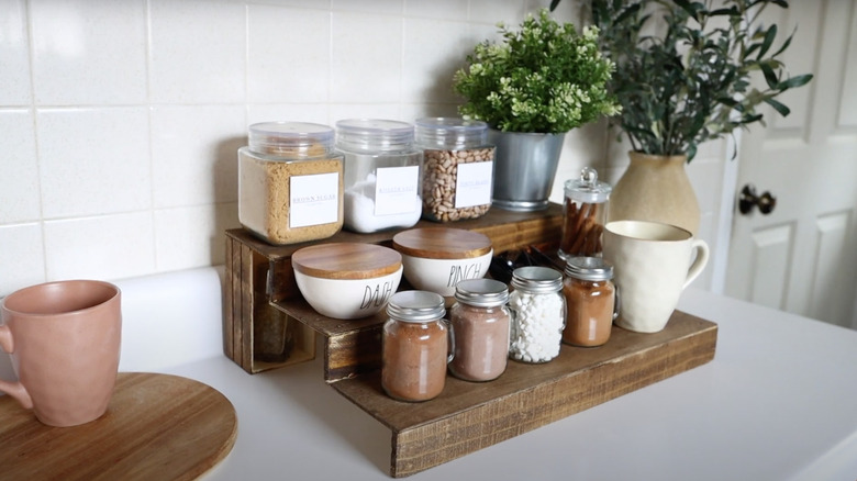 Spices, small potted plants, and tea mugs are organized on a wooden countertop shelf