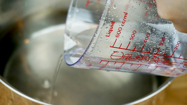 Pouring a measuring cup of water into a stainless steel pan