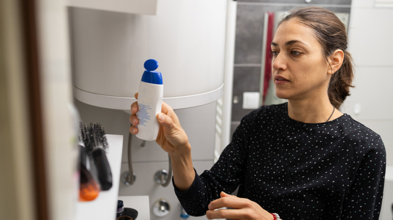A woman putting a shampoo bottle on a shelf in the bathroom