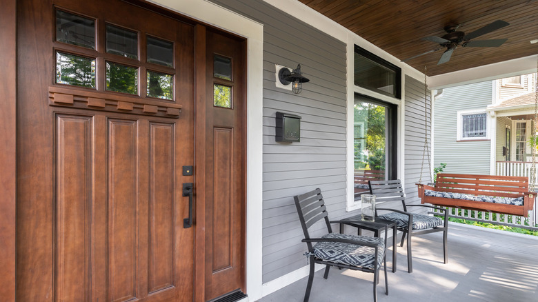 A front porch with metal table and chairs, and a wooden swing on the end that's in full view of the neighbor's house