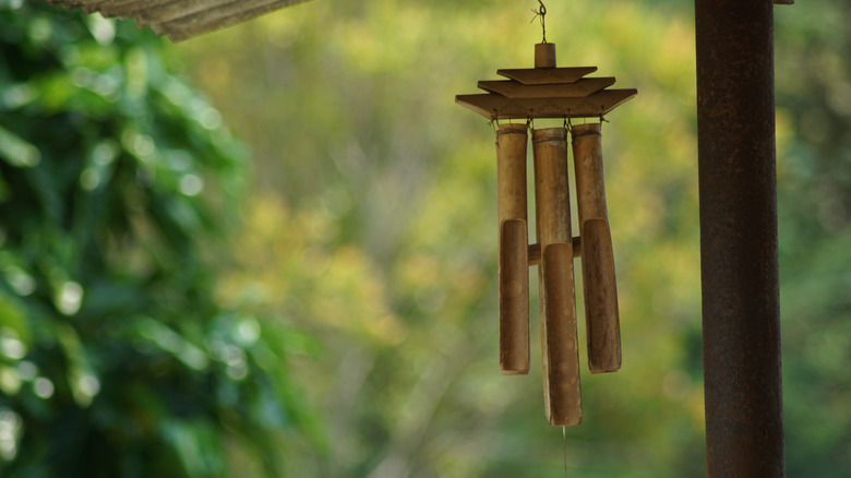 A simple wind chime made of bamboo hangs with blurred greenery in the background