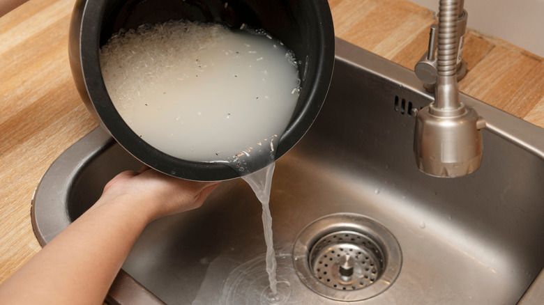 Hands dumping rice water down the drain in a sink from a black pot