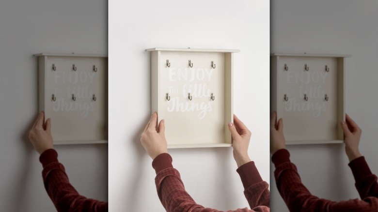 A woman hanging a custom key holder on the wall.