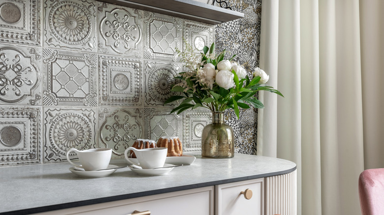 A kitchen with a soft gray countertop and textured vintage tile backsplash