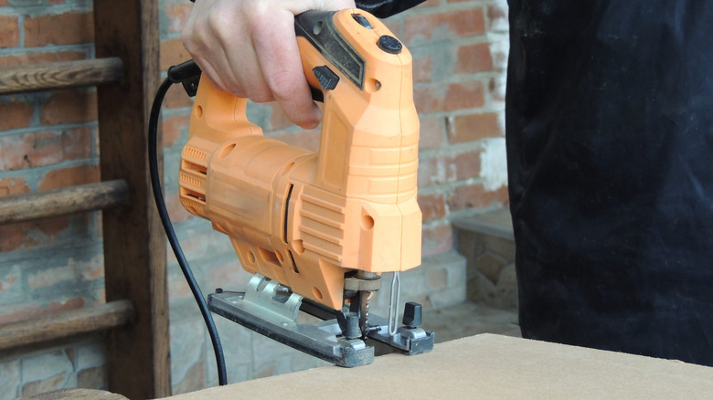 Person cutting through plywood with a corded jigsaw
