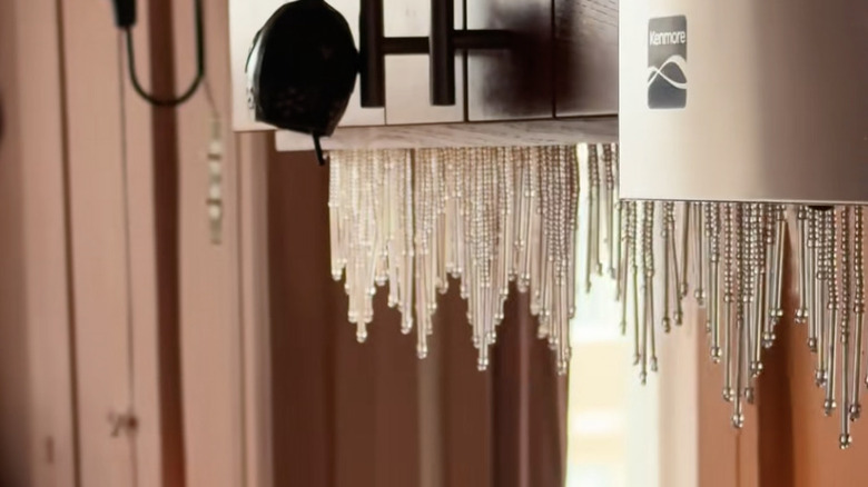 Beaded fringe hangs from brown kitchen cabinets.
