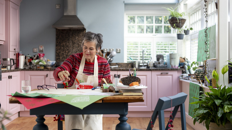 A woman sits at her kitchen table making some crafts.
