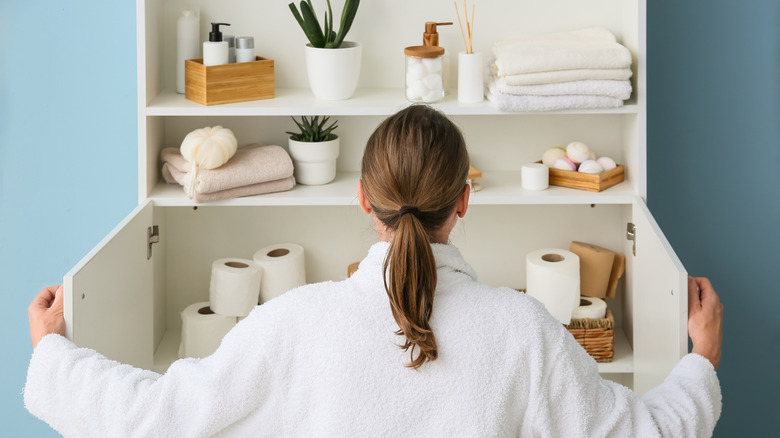 A woman looking inside a bathroom storage cabinet.