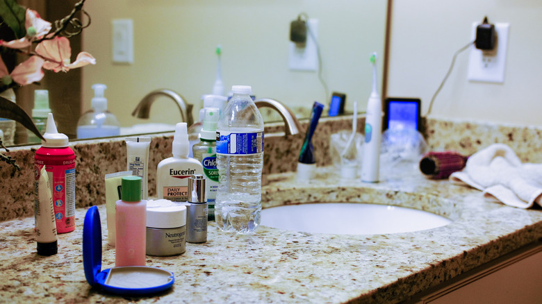 Cluttered bathroom countertop with beauty products and a water bottle