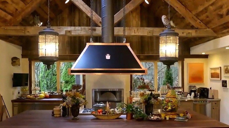Rachael Ray's farmhouse kitchen with a butcherblock island, and black exposed pipe range hood.