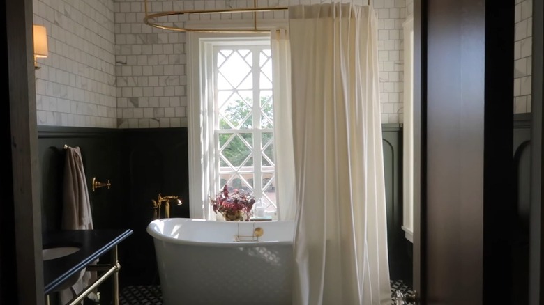 A white freestanding tub in the middle of the bathroom with an oblong metal rod and white curtain hanging from above.