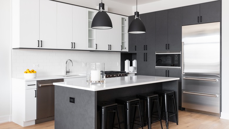 A modern kitchen with white and black cabinets, bar stools sitting at a large island, black pendant lights hanging over the marble countertop