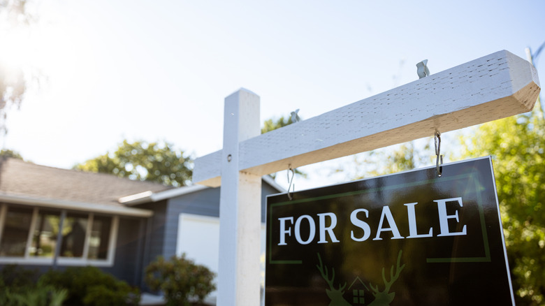 Close-up of a black and white for sale sign with a blurred house in the background