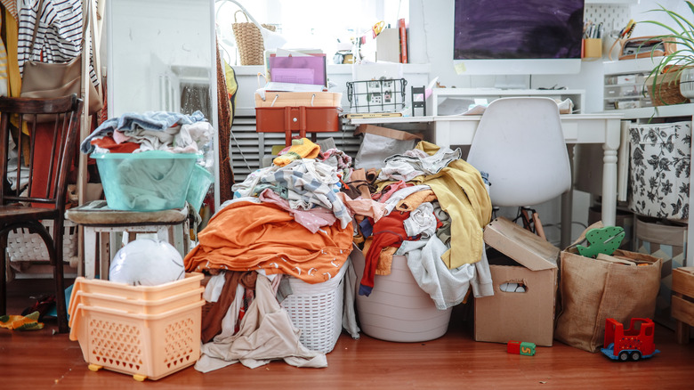 A messy home office covered in piles of laundry, kid toys, and other items