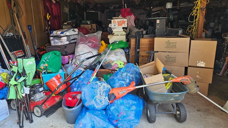 A cluttered garage with boxes, trash, and tools.