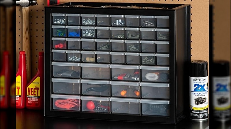 A black drawer organizer filled with small items in a garage.