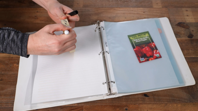 Person adding a label to a binder with seeds being stored in a page protector.
