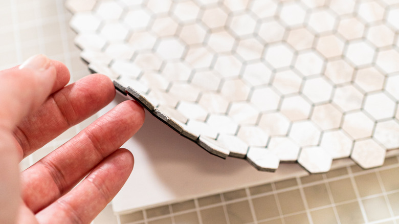 A man's hand peeling up honey comb shaped peel-and-stick tiles.