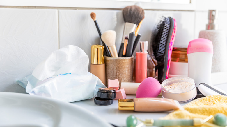 messy bathroom countertop with piles of beauty products and tools