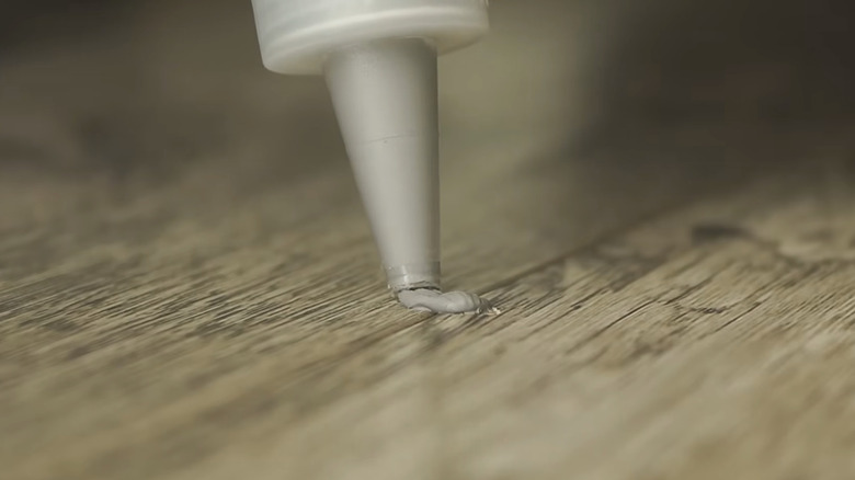 Applying putty to a chipped LVP floor.