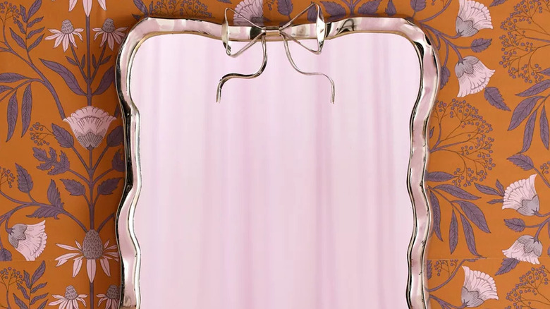 A silver mirror with a bow against floral wallpaper.