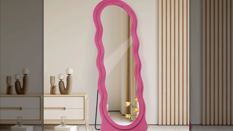 A hot pink squiggle mirror against a beige wall