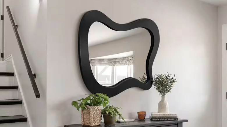A black asymmetrical mirror in a modern hallway.
