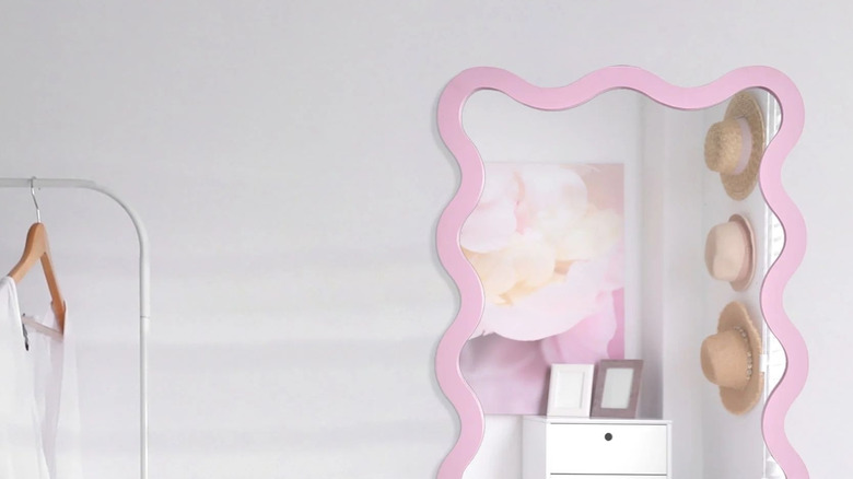 A pink squiggle mirror on a white wall.