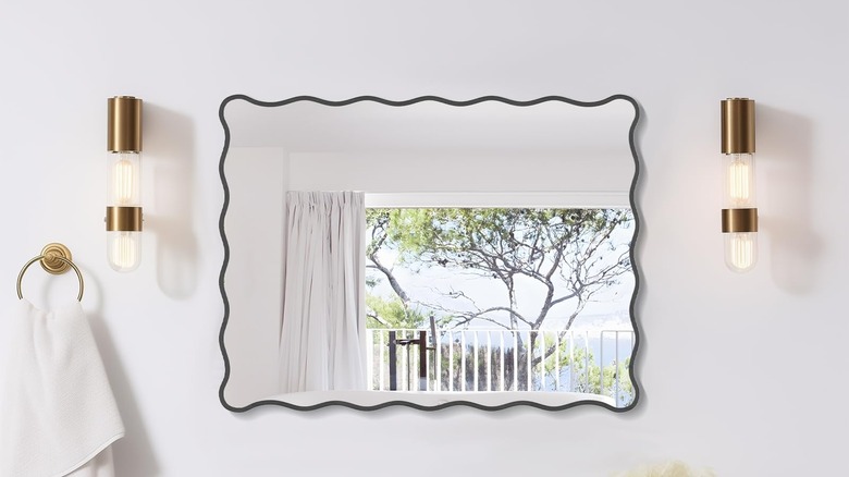 A wavy bathroom mirror with gold sconces.