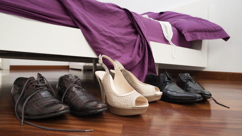 Three pairs of shoes sitting on the floor next to a bed with purple sheets