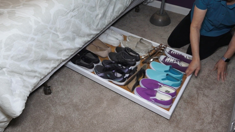 Person sliding a white shoe tray under a bed