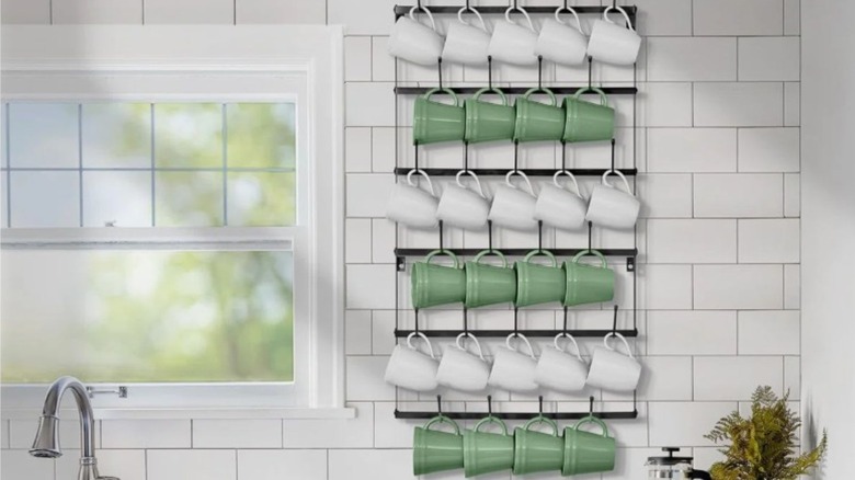 Cup rack filled with green and white coffee mugs on a tile wall
