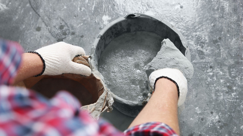 person with gloves on pouring cement in gray bucket